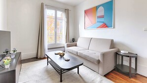 A living room with a sofa, a coffee table, a side table, and a painting on the wall. - Cosy Studio Asnieres (Asnières-sur-Seine)