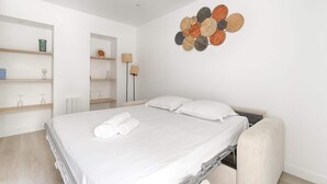 A modern hotel room with a neatly made bed, a bedside table with a lamp, and a wall-mounted decorative piece. - Modern Studio Near Paris w/ Fast WiFi, TV (Charenton-le-Pont)