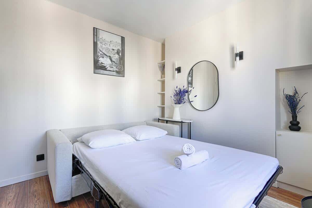 Une chambre à coucher moderne, avec un lit, une table de chevet, un miroir et une étagère murale agrémentée d’objets décoratifs.