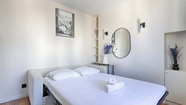 Een moderne slaapkamer met een bed, nachtkastje, spiegel en een wandplank met decoratieve objecten.