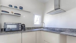 Een kleine keuken met een ingebouwde magnetron, koffiezetapparaat en een raam boven de gootsteen.