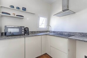 A compact kitchen with a built-in microwave, coffee maker, and a window above the sink. - Daumesnil Nation : Charming Lovely Studio (Paris)