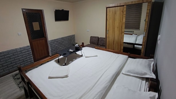 A hotel room with a large bed, a desk, a chair, a wardrobe, and a television. - Caravan Hostel (Tashkent)