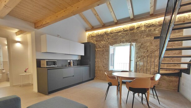 A modern kitchen with grey cabinets, a microwave, and a coffee maker. There is a dining area with a table and chairs, and a staircase leading to an upper level.