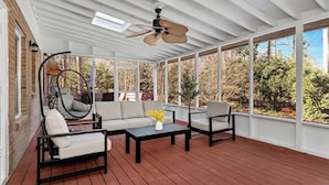 A covered patio with wooden flooring, a ceiling fan, and a seating area with a sofa and chairs.