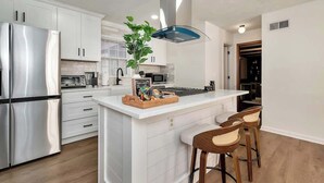A modern kitchen with white cabinetry, stainless steel appliances, and a central island with bar stools.