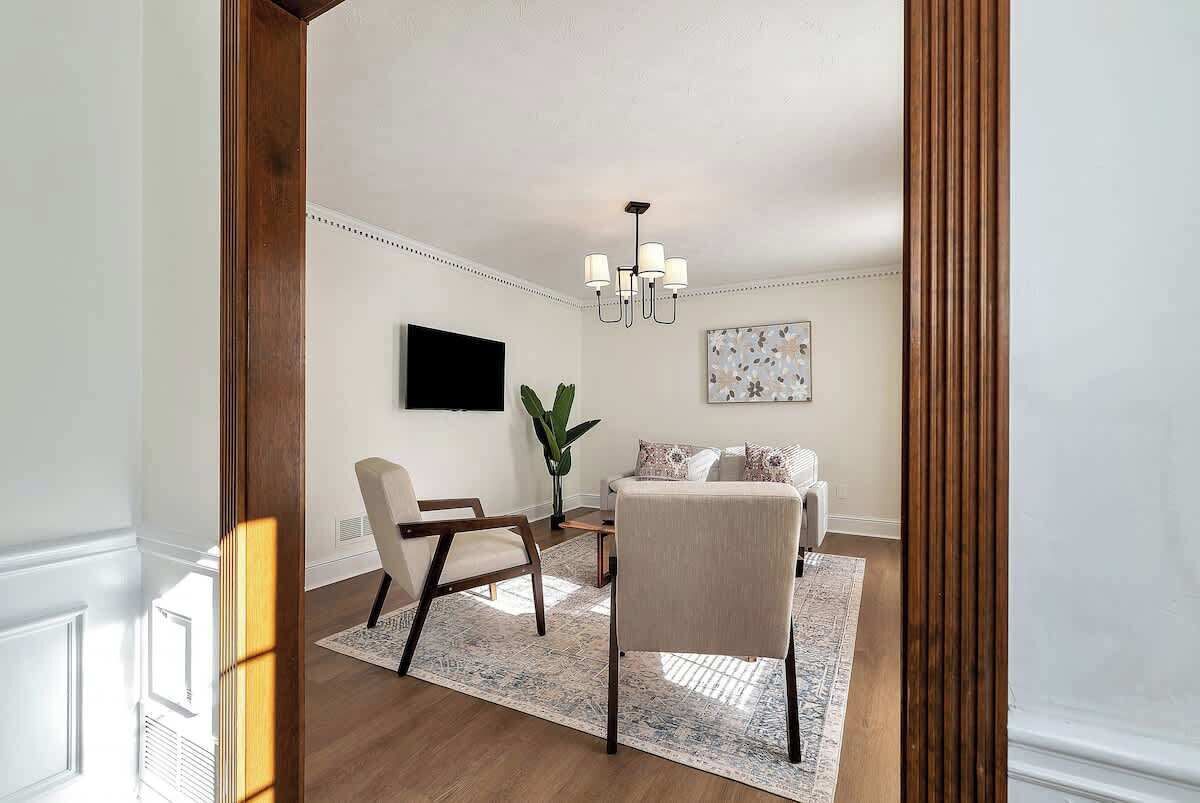 A modern living room with a sofa, a chair, a TV, and a chandelier.