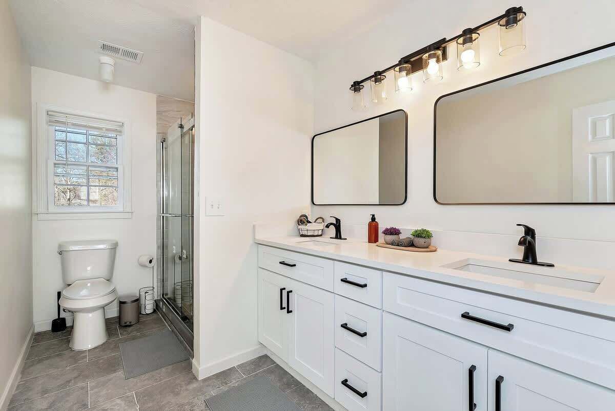 Een moderne badkamer met een wit wastafelmeubel, dubbele spiegels en een douchecabine van glas.