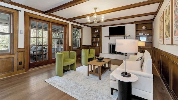 A spacious living room with wooden beams, a fireplace, and a large window overlooking a deck.