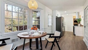 A dining area with a round table, chairs, and a hanging light fixture.