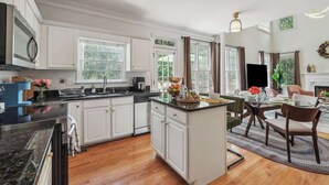 A modern kitchen with white cabinetry, a central island, and a dining area with a fireplace. - Chic Metro Family Stay / High Ceiling / Game Room (Lawrenceville)
