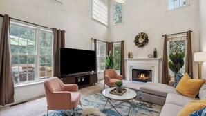 A spacious living room with a large TV, comfortable seating, a fireplace, and large windows. - Chic Metro Family Stay / High Ceiling / Game Room (Lawrenceville)