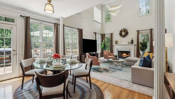 A spacious living room with a fireplace, a dining area with a glass table, and a cozy seating area with a sofa and armchairs. - Chic Metro Family Stay / High Ceiling / Game Room (Lawrenceville)