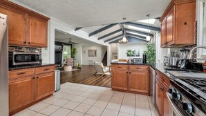 A spacious kitchen with wooden cabinets, a stainless steel refrigerator, a microwave, and a stove. There is a dining area with a chair and a table. - ALL Kings!/ Gameroom/ Huge Deck/ Family Friendly (Norcross)