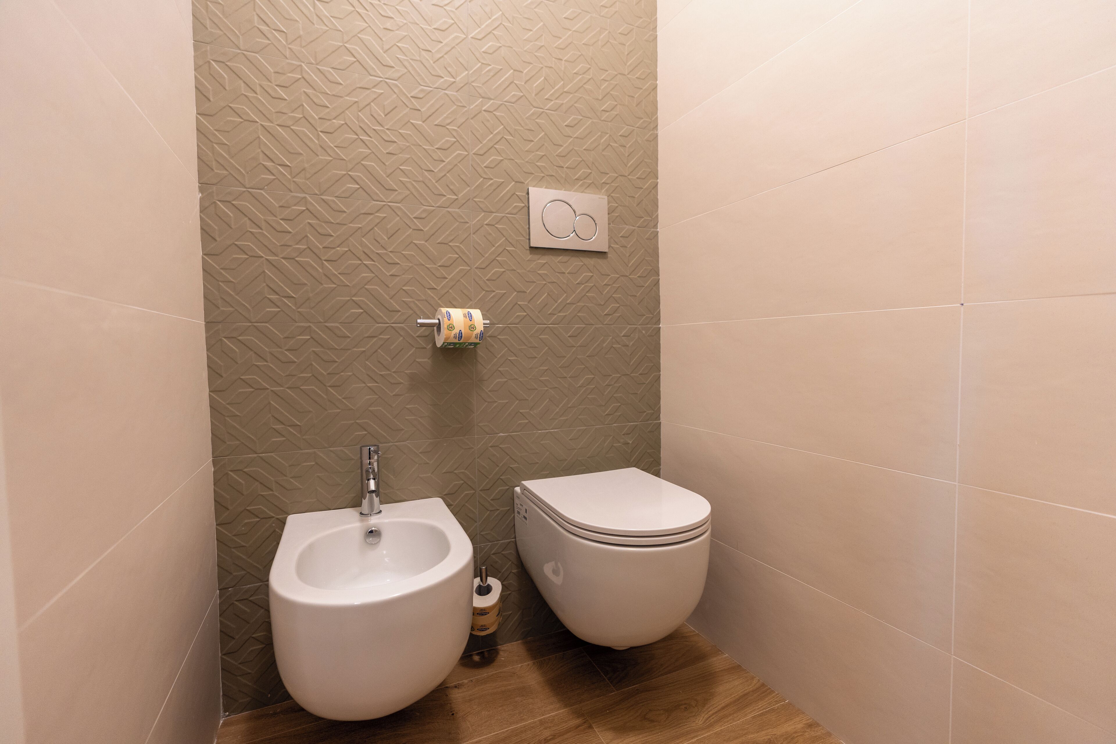 A small bathroom with a bidet, toilet, and a towel dispenser.