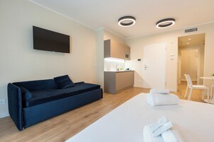 Una moderna camera d'albergo con divano letto, televisione a schermo piatto, angolo cottura e zona pranzo separata.