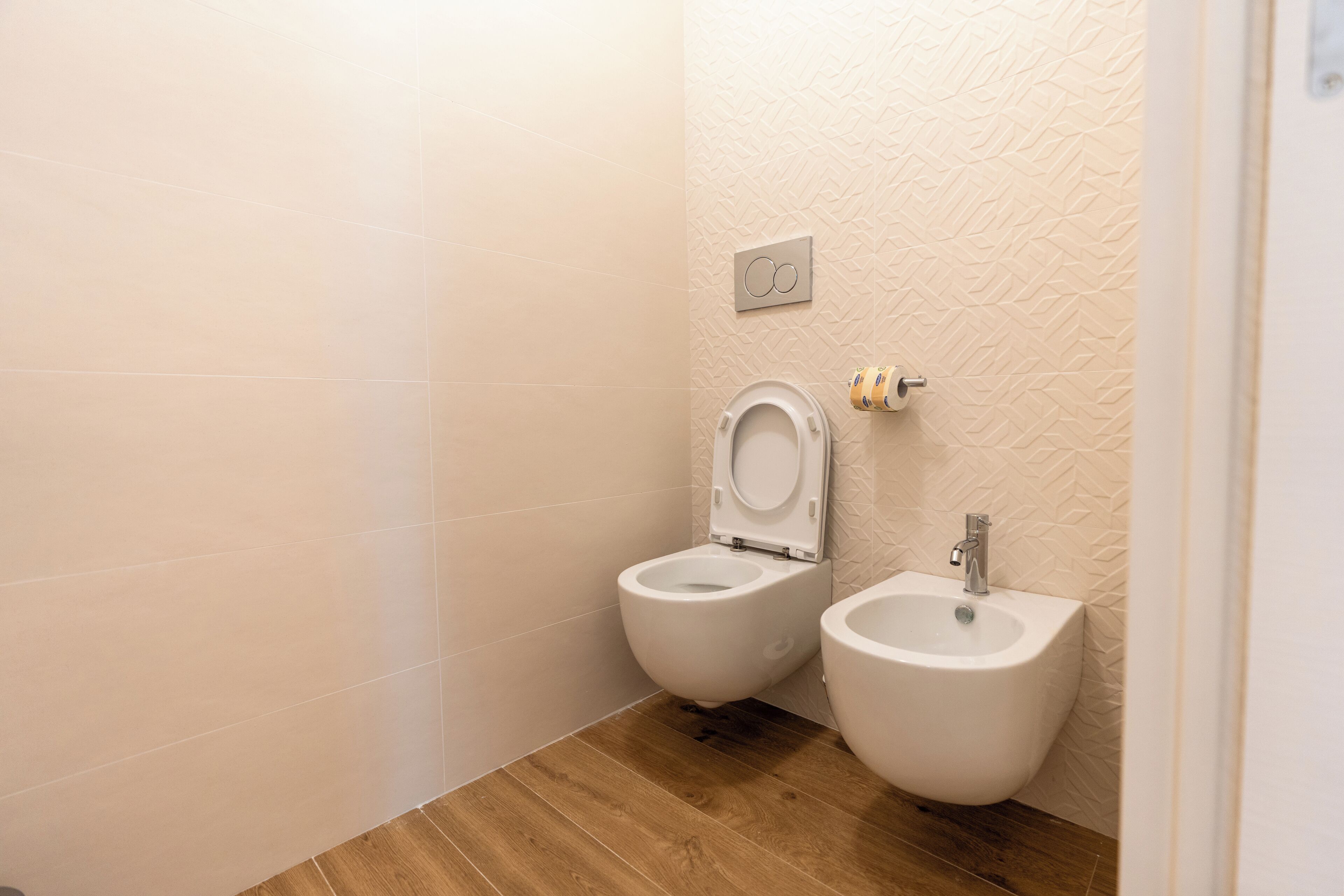 A bathroom with two toilets, a bidet, and a wall-mounted flush button.