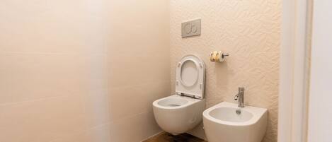 A bathroom with two toilets, a bidet, and a wall-mounted flush button.