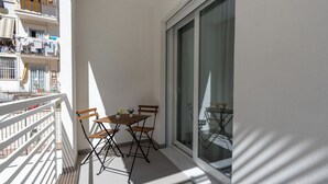 En balkon med et bord og stole, en skydedør samt udsigt til omkringliggende bygninger.