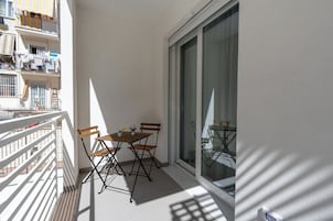 Un balcone con tavolo e sedie, una porta scorrevole in vetro e vista sugli edifici circostanti.