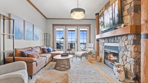 A cozy living room with a stone fireplace, a large TV mounted above it, and a comfortable seating area with sofas and a coffee table. - Equinoxe 152-3 Ski in/Ski out (Mont-Tremblant)