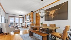 A spacious living area with a large wooden dining table, comfortable seating, and a fireplace. - Equinoxe 152-3 Ski in/Ski out (Mont-Tremblant)