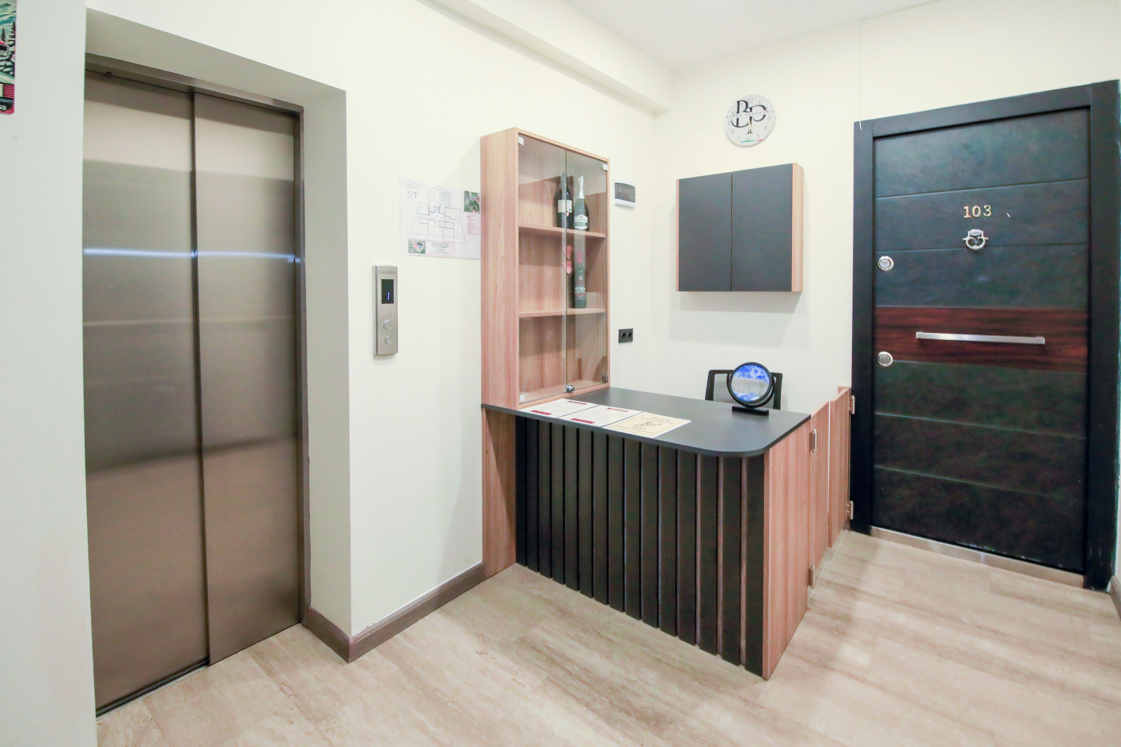A reception area with a wooden counter, a clock, and a door marked with the number 103.
