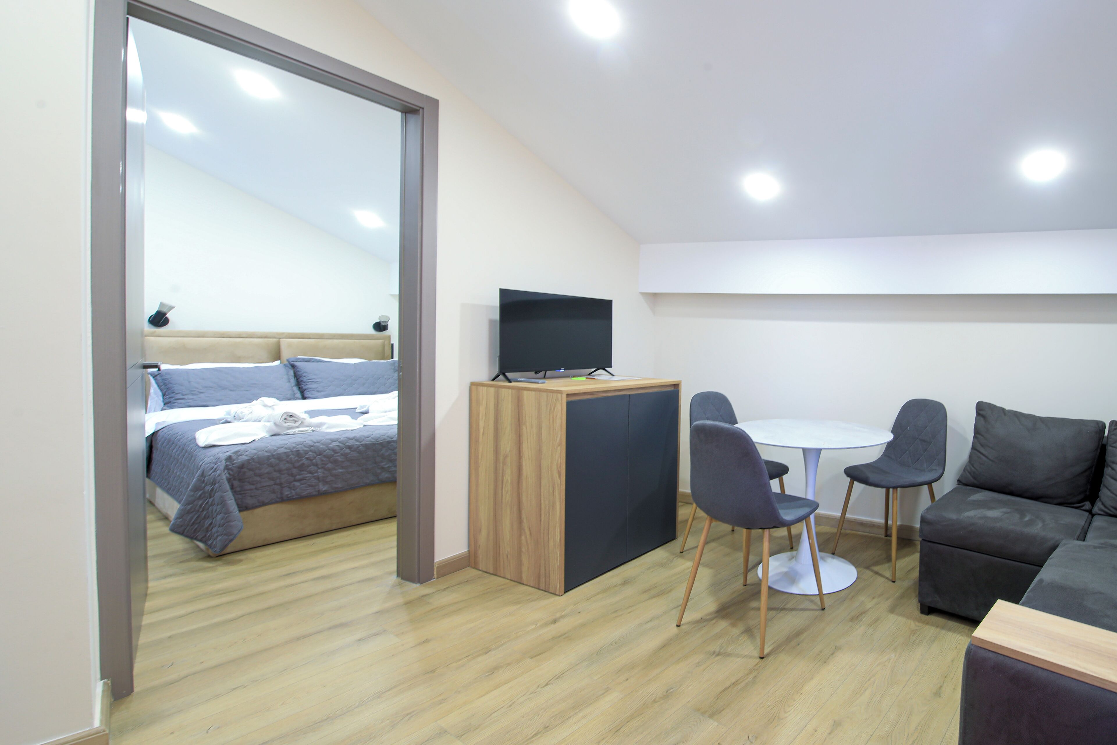 Habitación moderna con cama, escritorio con televisor, dos sillas, sofá y una mesita.
