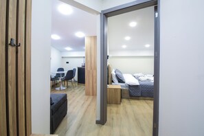 A modern room with a wooden floor, a bed with a gray quilt, a desk with a chair, and a small table with a lamp. - Babex Panorama (Bakuriani)