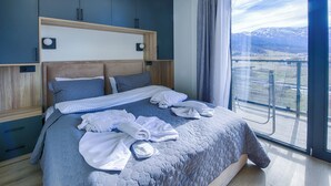 Een moderne slaapkamer met een groot bed, een houten hoofdbord en uitzicht op een bergachtig landschap door een groot raam.