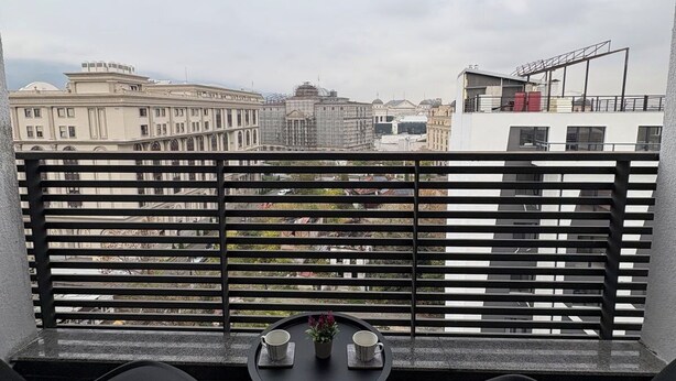A balcony with two black chairs and a small table with cups and a flower. - Aetheria apartment (Shkupi)