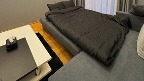 A modern bedroom with a large bed, a sofa, a small table, and a painting on the wall. - Aetheria apartment (Shkupi)