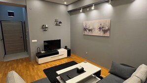 A modern living room with a grey sofa, a black coffee table, and a flat-screen TV. - Aetheria apartment (Shkupi)