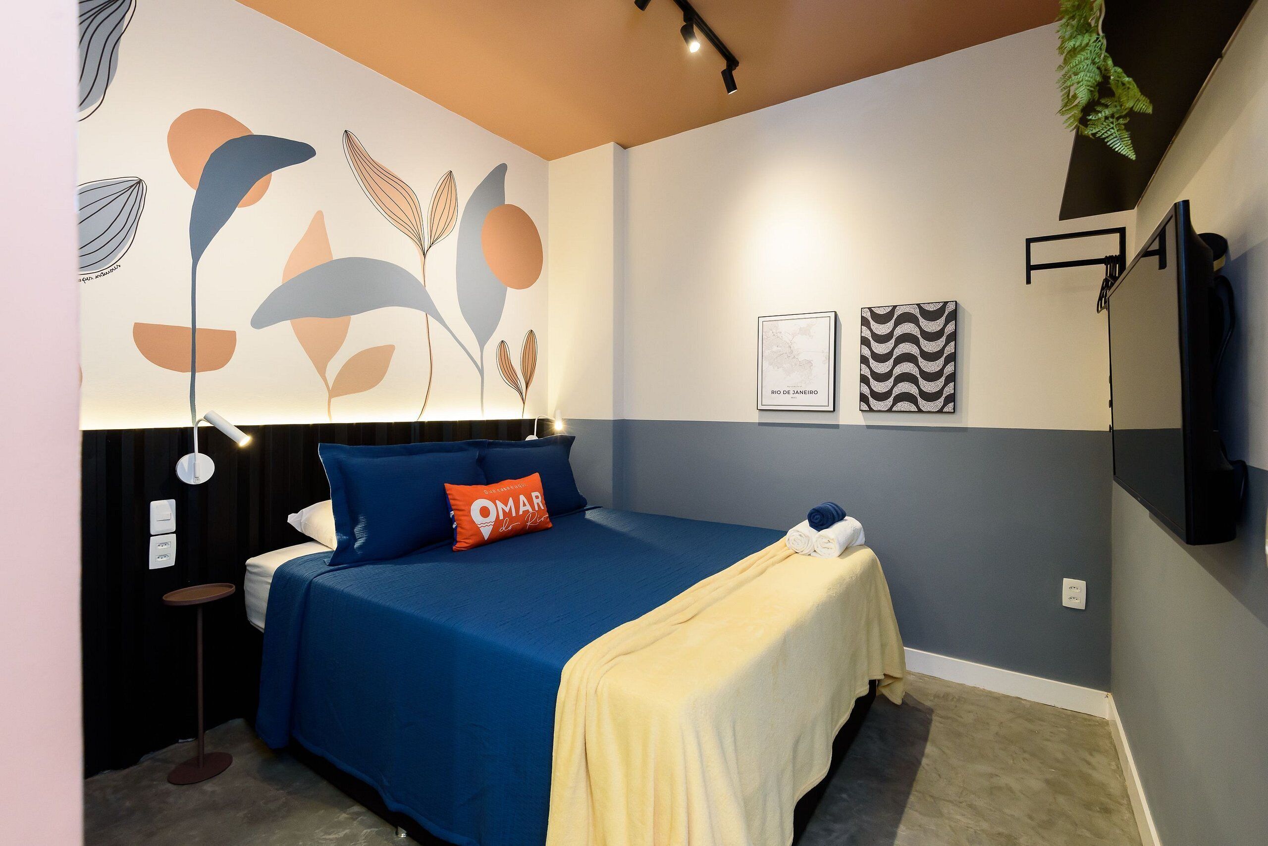 A modern hotel room with a bed, a bedside table, a wall-mounted TV, and a decorative wall with leaf patterns.