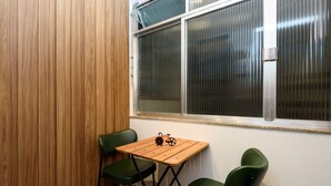 Una habitación pequeña con un separador de madera, una ventana con persianas, una mesa de madera con dos sillas verdes y una bicicleta como adorno sobre la mesa.