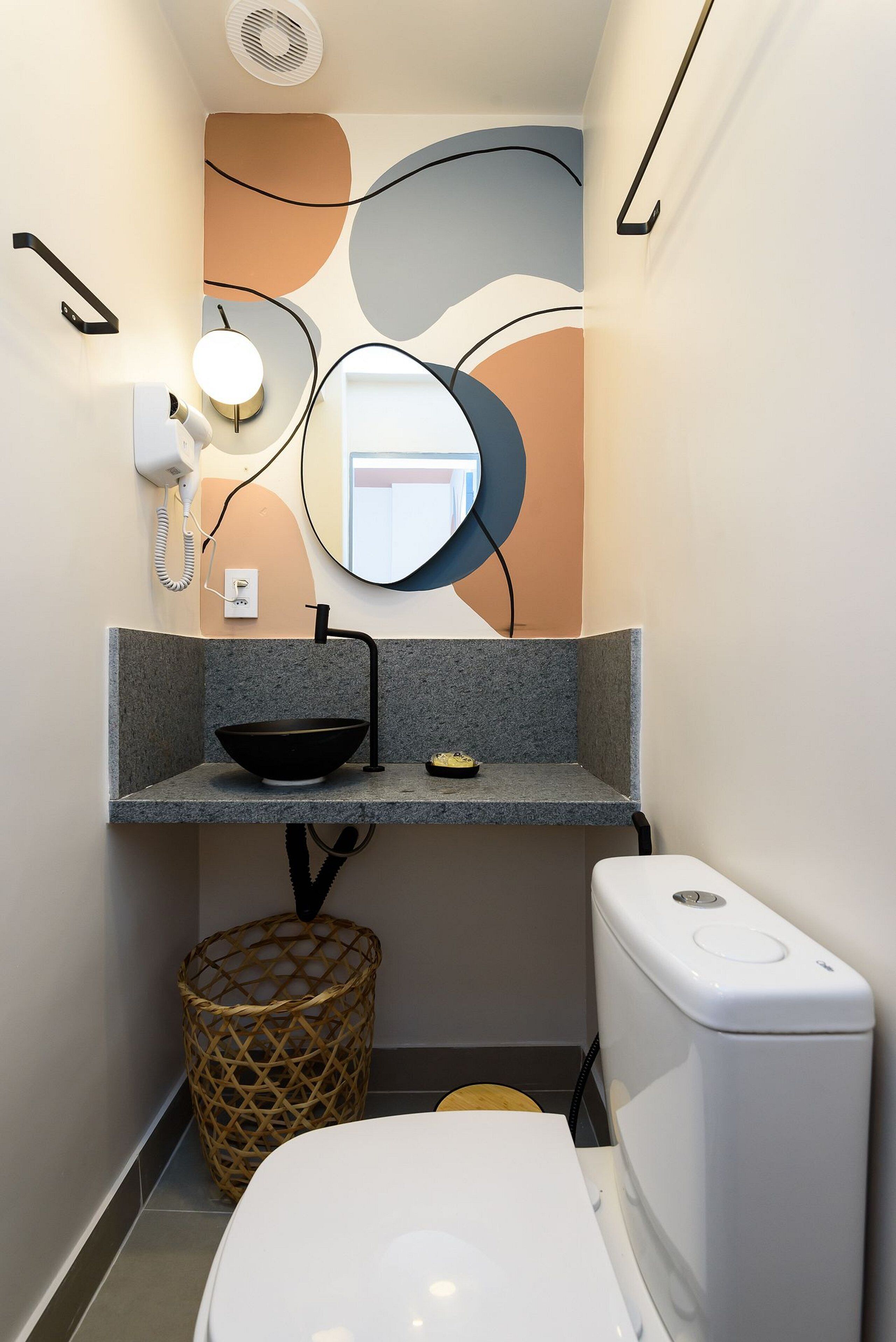 Un baño compacto de diseño moderno, con un espejo redondo, un lavabo negro y un inodoro blanco.