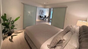 A modern bedroom with a large bed, a bedside table with a lamp, and a potted plant. - Bright, warm & spacious 1 BR in North End Halifax (Halifax)