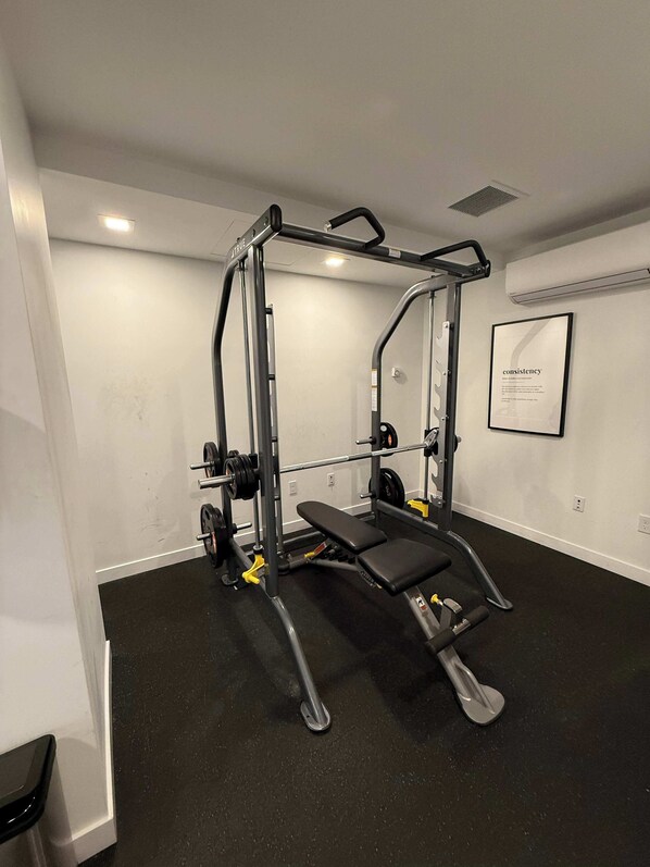 A gym with a squat rack, bench press, and weight plates. - Bright, warm & spacious 1 BR in North End Halifax (Halifax)