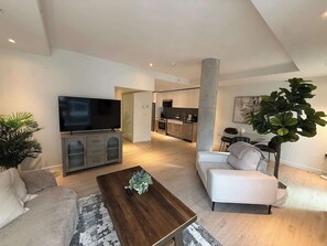 A modern living room with a flat-screen TV, a sofa, a coffee table, and a large plant. - Bright, warm & spacious 1 BR in North End Halifax (Halifax)