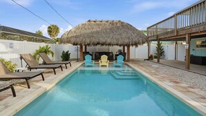 Une piscine avec des chaises longues et une structure dotée d’un toit de chaume.