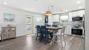 Une cuisine moderne avec des meubles blancs, un coin repas avec des chaises bleues et une table à manger en bois.