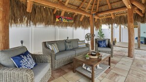 Un espace extérieur abrité avec des meubles en osier, une table en bois et un panneau indiquant « Pirates des Caraïbes ».