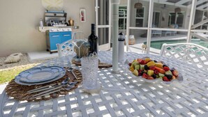 Ein Essbereich im Freien mit einem Tisch für zwei Personen, einem Grill und einem Pool im Hintergrund.