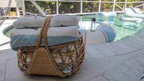 Ein Korbbad mit gefalteten Handtüchern und einer Flasche auf einer gefliesten Terrasse in der Nähe eines Pools.