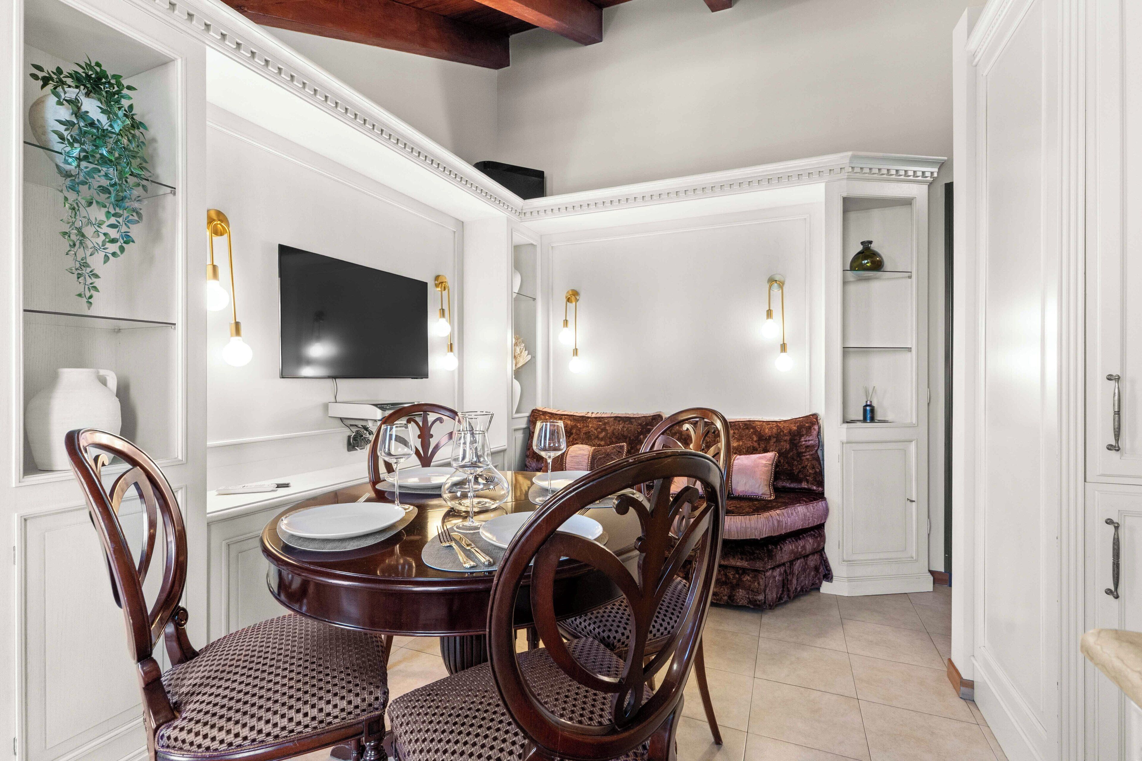 A dining area with a round table, chairs, and a television mounted on the wall.