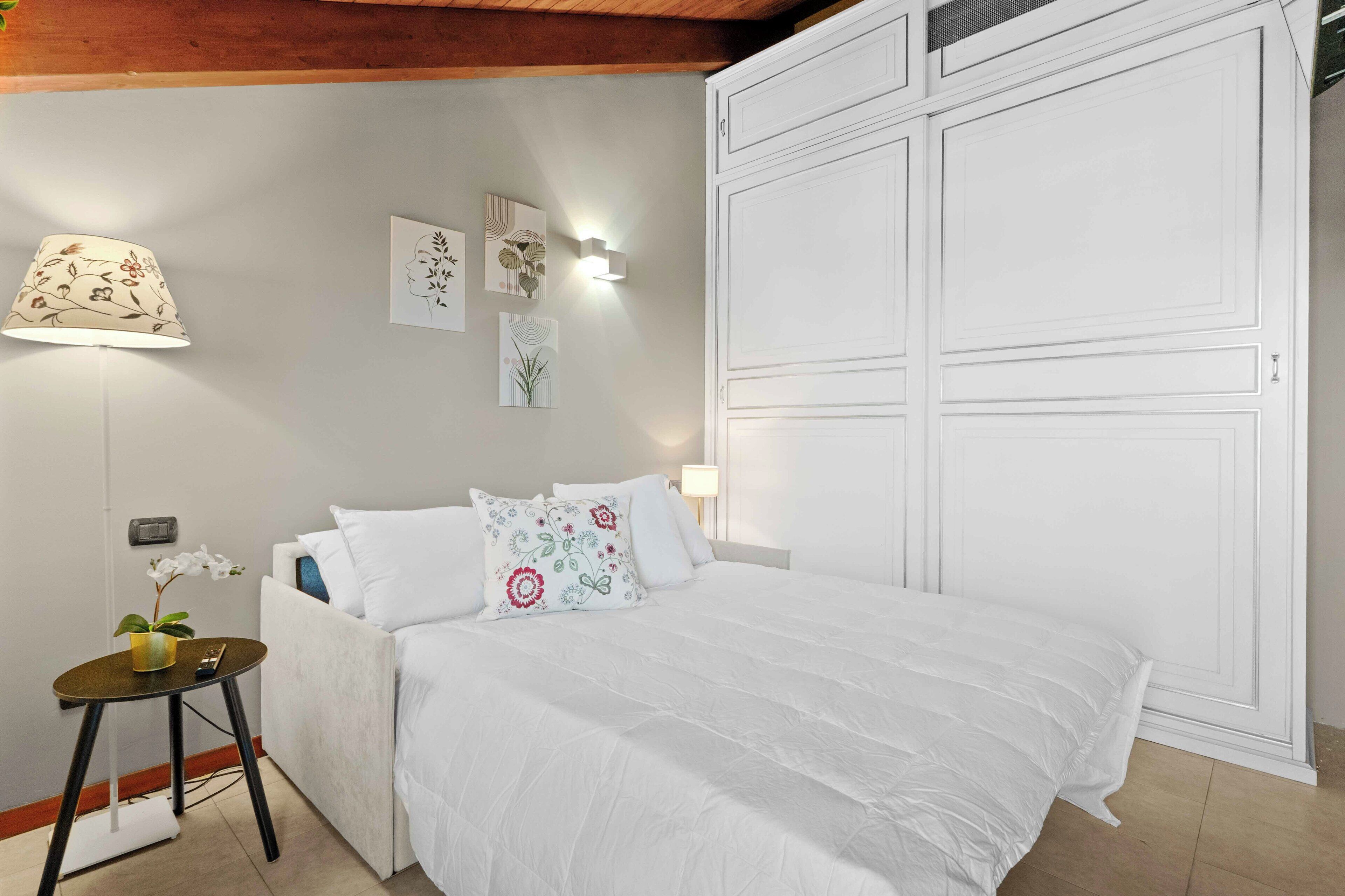 A neatly arranged bedroom with a bed, bedside table, lamp, wall art, and a wardrobe.