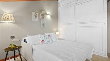 A neatly arranged bedroom with a bed, bedside table, lamp, wall art, and a wardrobe.