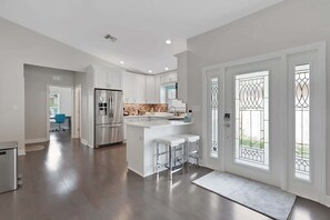 A modern kitchen with white cabinetry, a stainless steel refrigerator, and a central island with bar stools. - Stunning 4BR Home w/ Heated Pool & Spa- Near Beach (Naples)