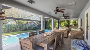 Une terrasse couverte avec une piscine, des meubles en bois, des ventilateurs de plafond et une vue sur le jardin arrière.