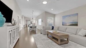 Un vaste espace de vie comprenant un canapé blanc, une table basse en bois et un ventilateur de plafond.